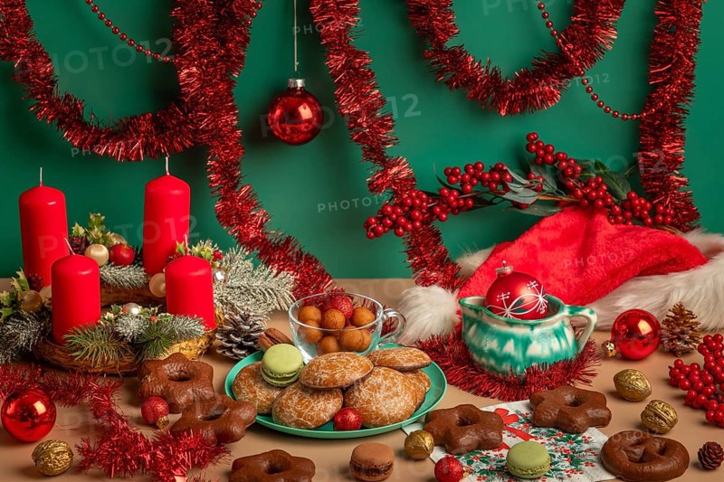 Table with Christmas decorations, biscuits and Advent wreath with red candles, framed by garlands