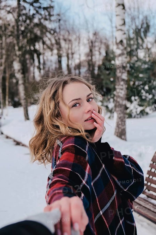 Curly blond pretty young woman in poncho in winter park. Cold weather. Holidays, season and leisure concept. Christmas, New year. Winter fashion, holidays, rest, travel concept