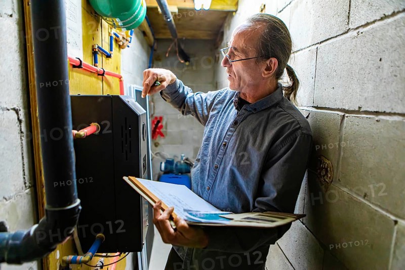 Middle aged home Inspector is visiting the equipment technical room during an inspection. Caucasian man inspects plumbing and electricity with notebook