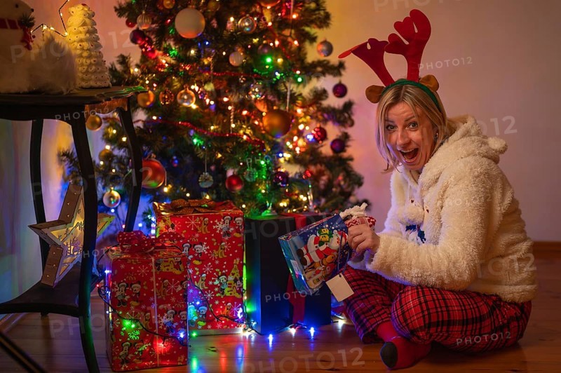 A woman in a Christmas costume opens a present under the Christmas tree