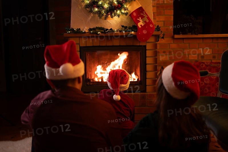 Family wearing Santa Claus hats sitting in front of the fireplace. Poland