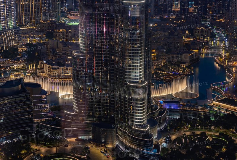 A picture of the Dubai Fountain Show, at night, and the bottom of the Burj Khalifa, next to other Downtown Dubai buildings