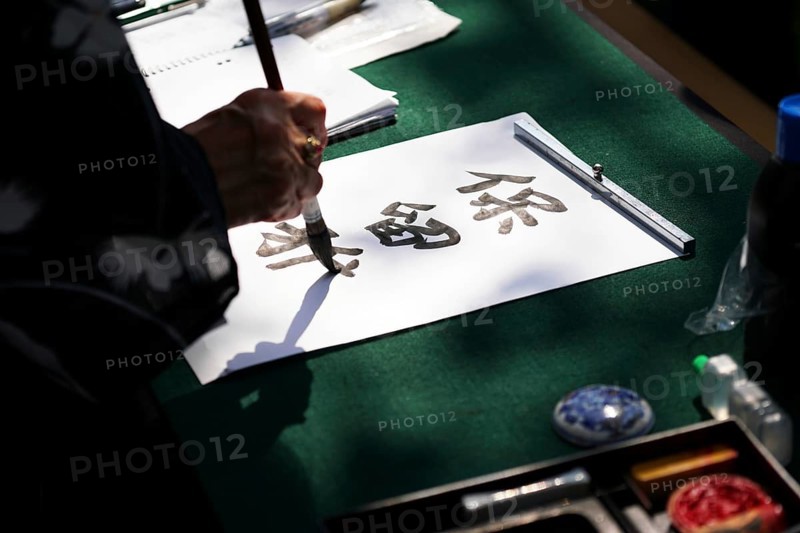japanese calligraphy, unrecognizable person writing kanji characters with ink brush on paper, english translation: reserved