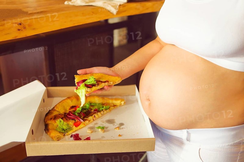Young pregnant woman eating pizza at the kitchen. Pregnant nutrition