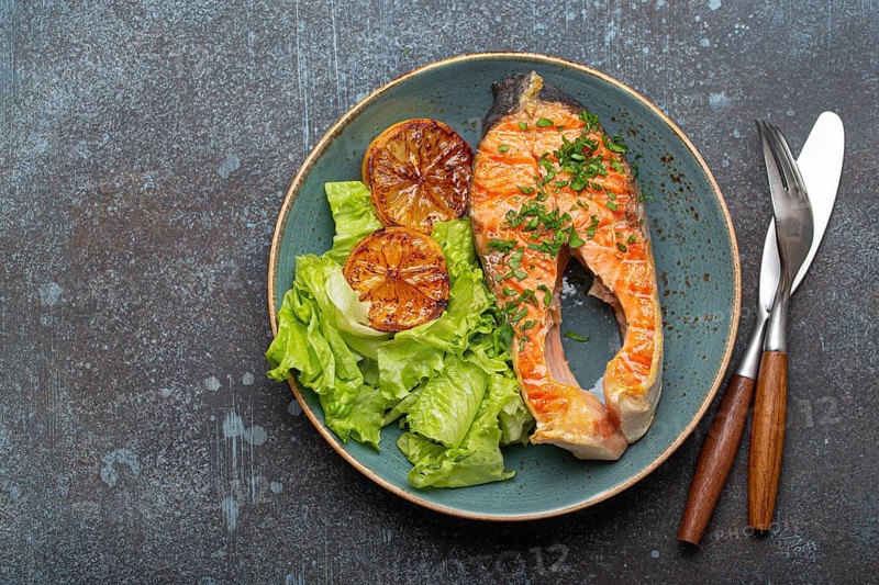 Grilled fish salmon steak and green salad with lemon on ceramic plate on rustic blue stone background top view, balanced diet or healthy nutrition meal with salmon and veggies, space for text, food photography, food photography