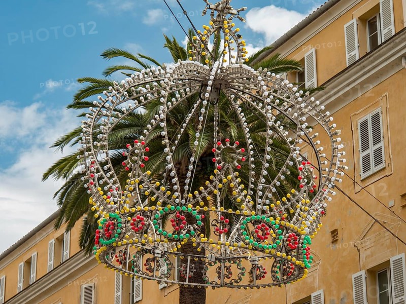 Colourful crown of pearls as decoration on a palm tree in front of a yellow building and blue sky, Ajaccio, Corsica, Mediterranean Sea, France, Europe