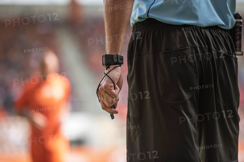 Hand of soccer referee with wristwatch and whistle.