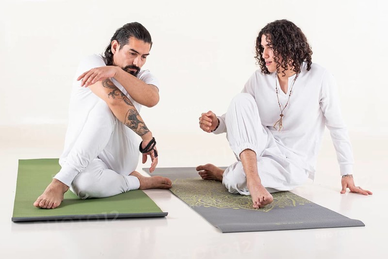 A yoga instructor is teaching yoga to a young man. Both dressed in white yoga clothes. Front view