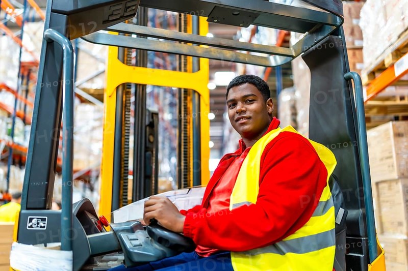 Side view of a happy latin american worker driving forklift in a storage warehouse