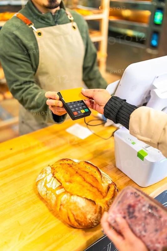 Vertical cropped photo of the hands of a woman paying using credit card in a modern bakery