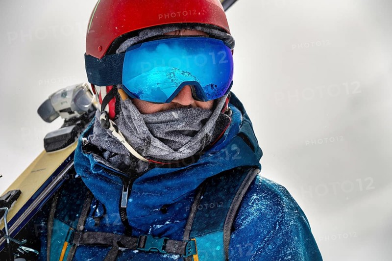 Closeup portrait of ski goggles of a man with reflection of snowy mountains. The mountain range is reflected in the ski mask. Portrait of a man in a ski resort against the backdrop of mountains and sky in a snow blizzard