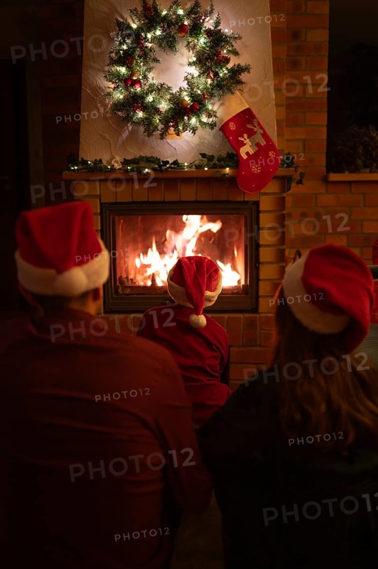 Family wearing Santa Claus hats sitting in front of the fireplace. Poland