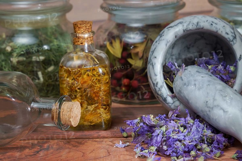Crushing medicinal plants in a mortar and pestle with different homeopathic preparations in the background