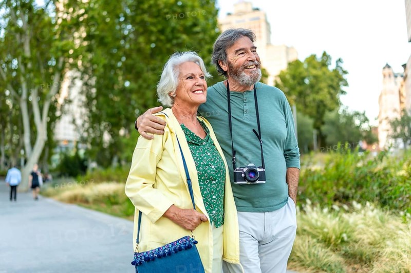 Mature caucasian man with a camera and wife visiting an urban park walking together
