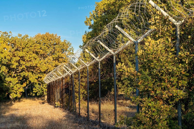 A view of a tall fence with barbed wire leading through forest on the border of Turkey and Bulgaria