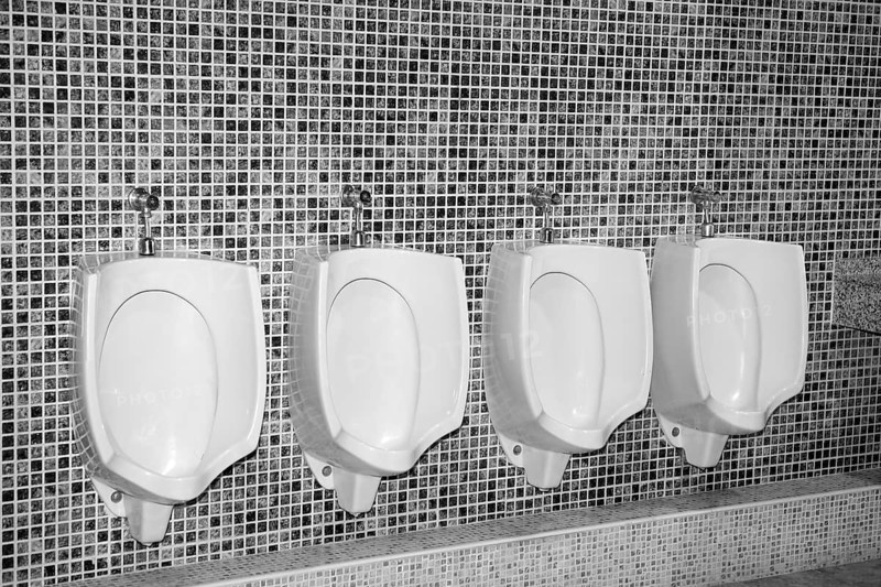 Bathroom urinal in a row with gray tiles black and white