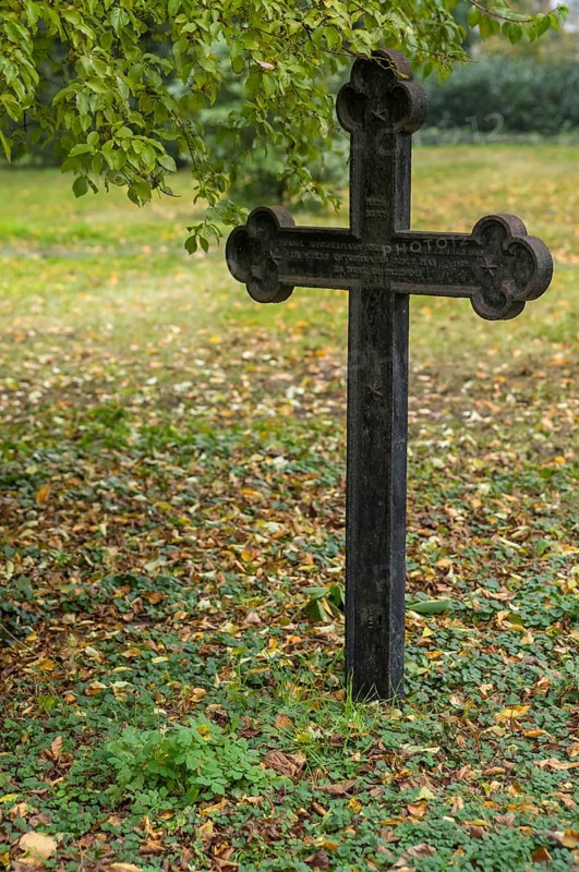 Weathered iron cross marking a grave in a cemetery during the fall season