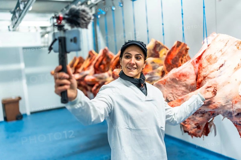 Caucasian adult female vlogger talking to audience recording inside the cold storage room in a meat factory