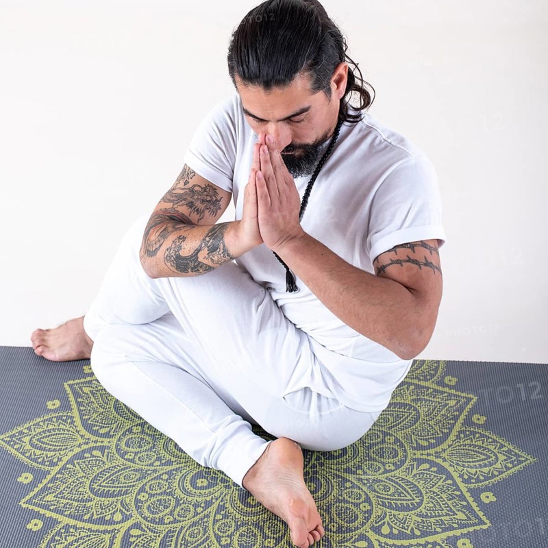 A man dressed in white doing yoga on a mat over white background. High angle view