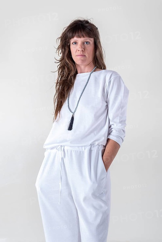 Portrait of a woman dressed in white yoga clothes over white background wearing a japa mala while looking at camera. Studio shot
