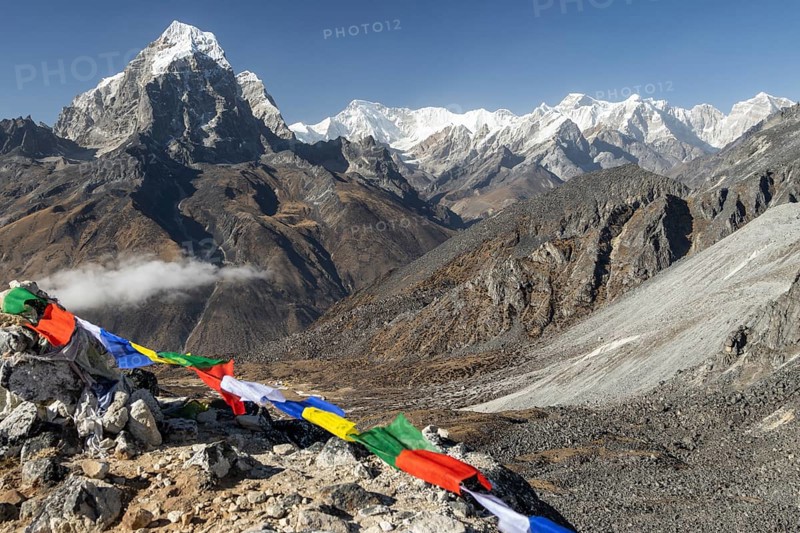 The eight-thousander Cho Oyu, Tenzing Peak and Hillary Peak honouring Sir Edmund Hillary and Tenzing Norgay Sherpa, Taboche Peak and Gyachung Kang, the highest mountain below eight-thousand metres seen among many other Himalayan peaks from a glacial moraine high above Ama Dablam Base Camp in Khumbu, the Everest Region of the Himalayas. Some Buddhist prayer flags in the foreground. Post-monsoon, autumn trekking season. Sagarmatha National Park, a UNESCO World Heritage Site. Solukhumbu, Nepal, Asia