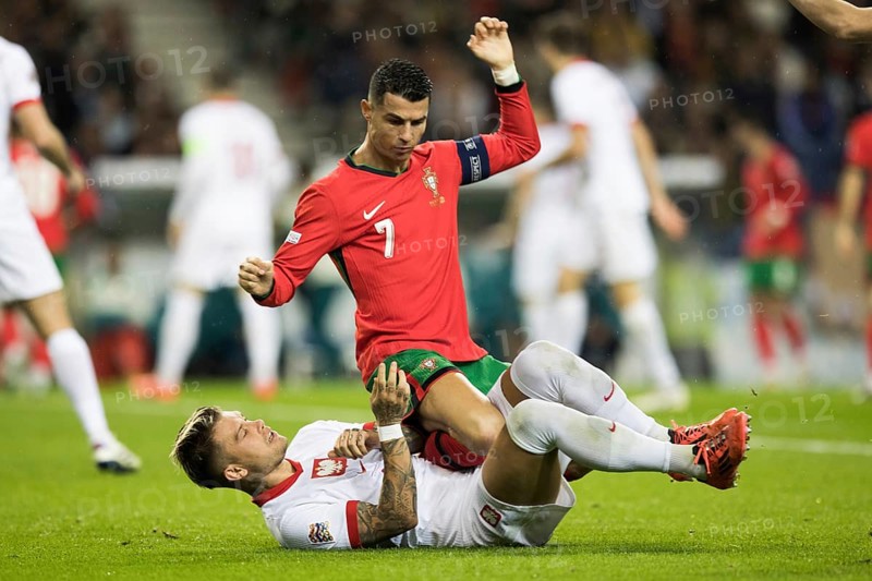 Football match, captain Cristiano RONALDO CR7 Portugal on the stomach and partly on the abdomen of Kamil PIATKOWSKI Poland kneeling with his right arm and captain's armband pointing upwards and looking down at his opponent, Kamil PIATKOWSKI Poland lying on the ground on the grass with his legs screaming upwards, Estadio do Dragao, Porto, Portugal, Europe