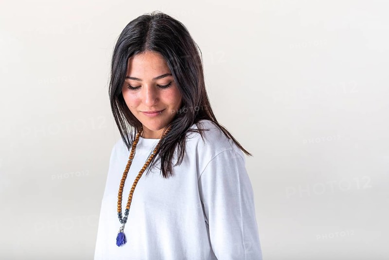 Portrait of a young woman dressed in white yoga clothes over white background wearing a japa mala. Studio shot