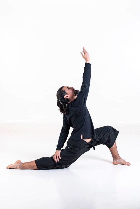 A man dressed in black doing yoga over white background. anjaneyasana yoga pose. Studio shot