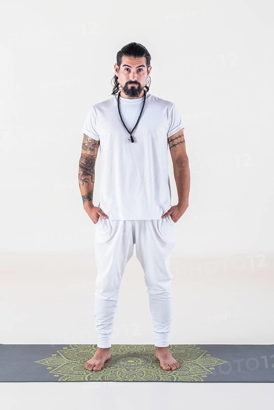 Portrait of a man dressed in white yoga clothes over white background while looking at camera. Studio shot