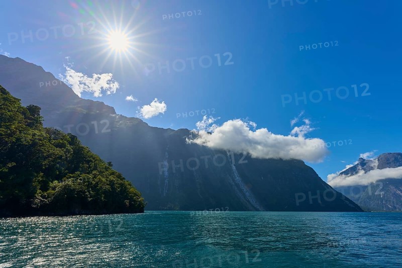 Clear sun over a fjord, surrounded by majestic mountains and a slightly cloudy sky, summer, Milford Sound, Te Anau, Fiordland National Park, South Island, New Zealand, Oceania