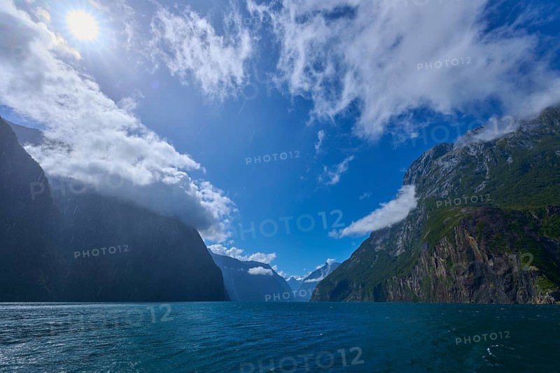Sunlit mountains surrounded by deep water and clouds, summer, Milford Sound, Te Anau, Fiordland National Park, South Island, New Zealand, Oceania