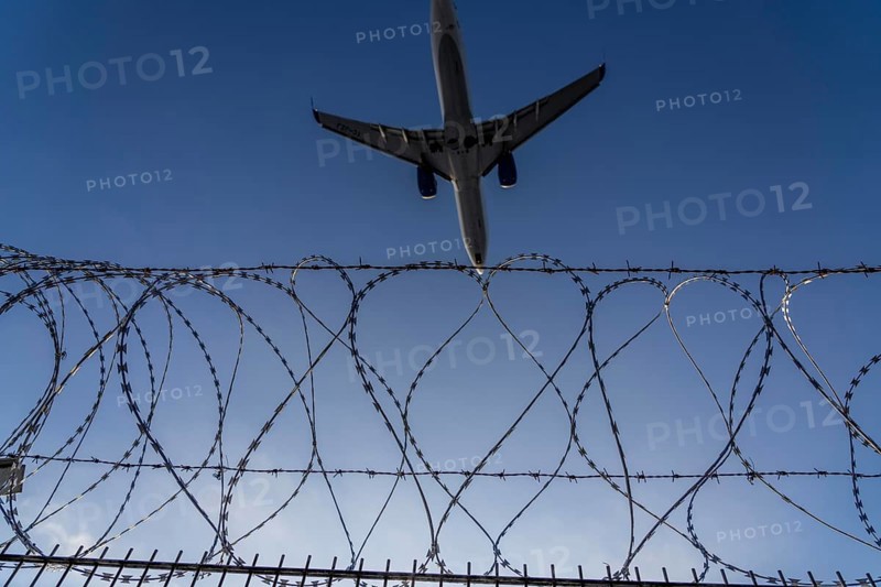 Symbolic image security at the airport, outer fence at Düsseldorf International Airport, steel wire fence, with S-wire rolls, NATO wire, on the top of the fence, aeroplane approaching, sunset, North Rhine-Westphalia, Germany, Europe