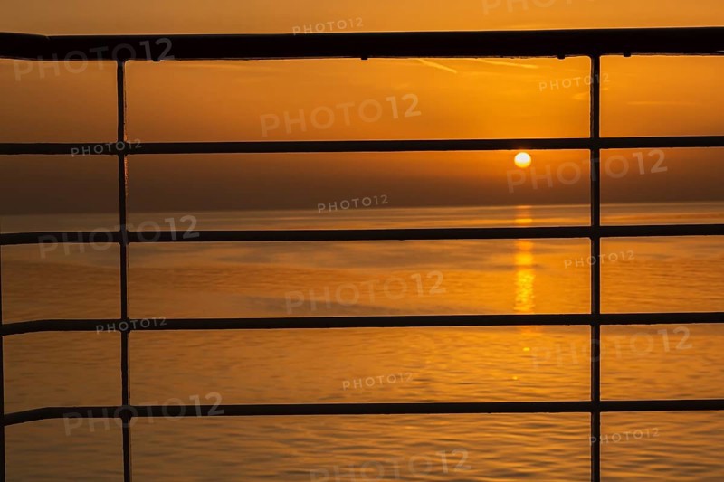 Close-up of silhouetted railing on cruise ship and golden setting sun over Adriatic sea near Zadar, Croatia in summer