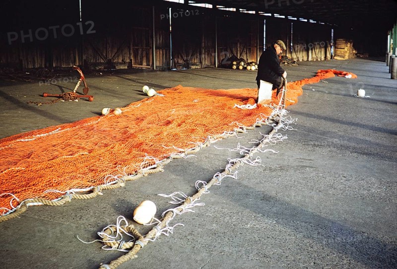 Man sitting in a storage shed mending a fishing net, unspecified location, Great Britain 1975