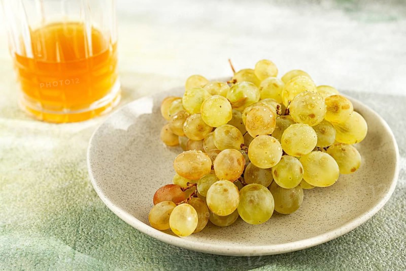 A branch of white grapes, on a gray plate, with a glass of white wine, top view, natural light, food concept, no people