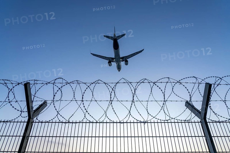 Symbolic image security at the airport, outer fence at Düsseldorf International Airport, steel wire fence, with S-wire rolls, NATO wire, on the top of the fence, aeroplane approaching, sunset, North Rhine-Westphalia, Germany, Europe