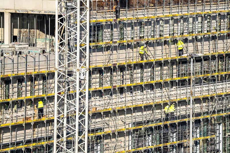 Large construction site, scaffolded new building, factory and office building, workers on the scaffolding during facade work