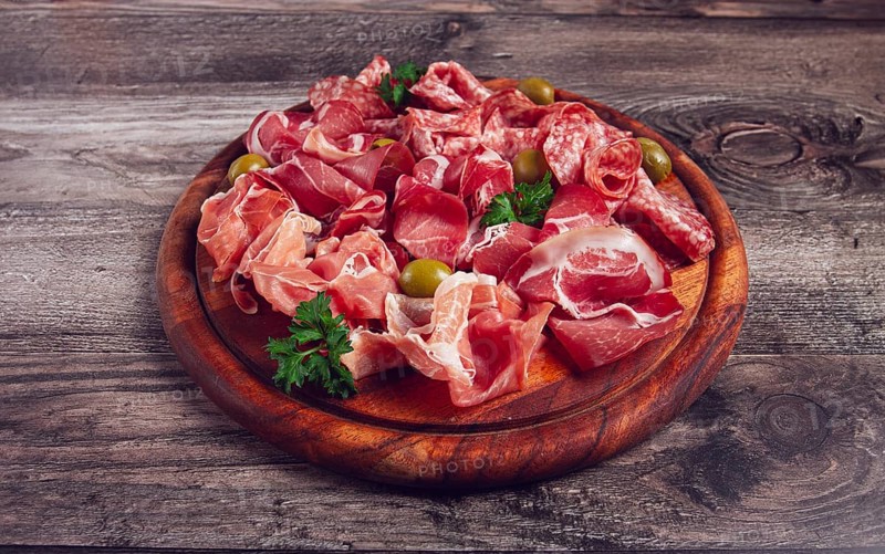 Assortment, sliced meat appetizer, prosciutto, salami and ham, with olives, on a wooden board, breakfast, top view, close-up, no people