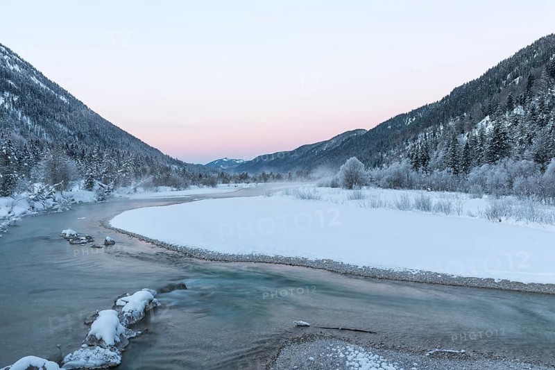Isar valley in winter at temperatures of minus 18 degrees Celsius. Snow covered landscape with the Isar river flowing through. Some hoar frosted trees. Early morning at sunrise