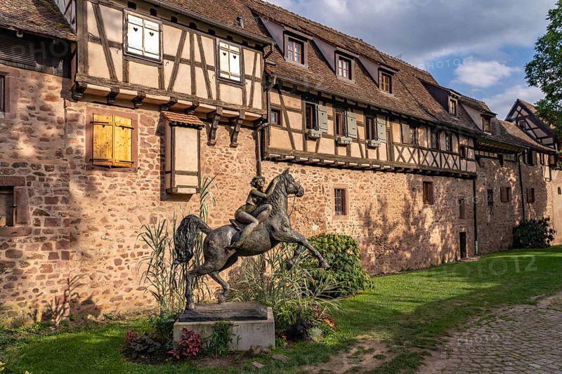 Statue of a woman on horseback with horse La Dame du Parc by the artist Josepha and half-timbered houses of the town wall of Riquewihr, Alsace, France, Europe