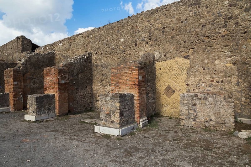 Remnants of old terracotta brick and stone wall structure plus numbered columns with white marble bases at the ancient ruins of Pompeii, Campania region, Italy, Europe