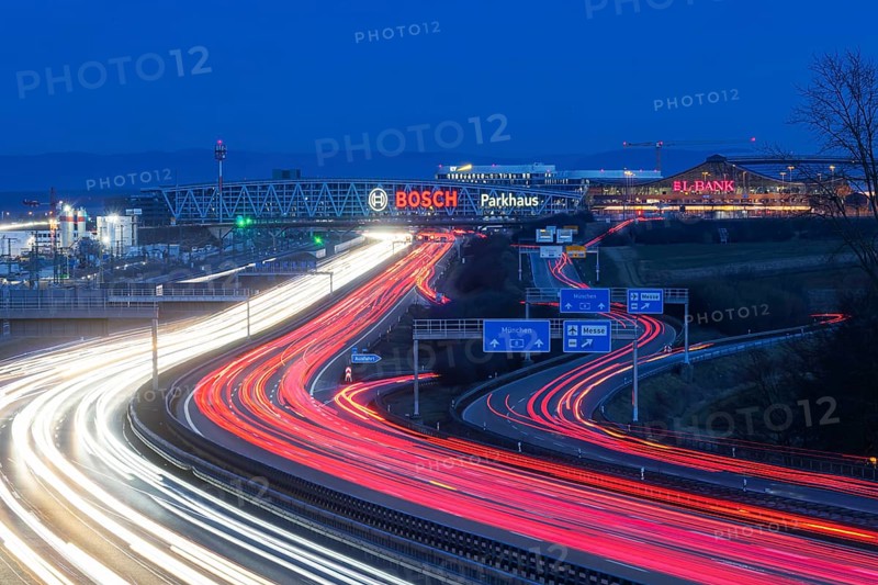 A8 motorway at Stuttgart Airport in the evening. Heavy traffic, lanes of light. Modern architecture of Messe Stuttgart with multi-storey car park above the motorway lanes. Logo of the Bosch company. Stuttgart, Baden-Württemberg, Germany, Europe