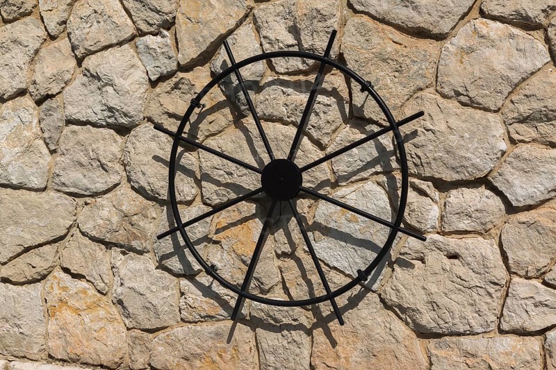 Close-up of black metal replica of a ship's helm displayed on exterior beige and tan stone wall of Maritime Police station building, Port of Gruz, Dubrovnik, Croatia, Europe