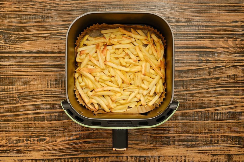 Freshly cooked golden french fries are in an air fryer, showcasing their crispy texture