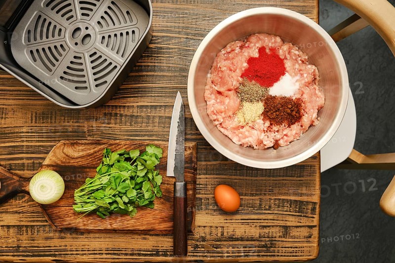 Ground meat is mixed with various spices, fresh cilantro, and chopped onion on a wooden cutting board. An egg and a knife are also present, indicating preparation for a delicious meal