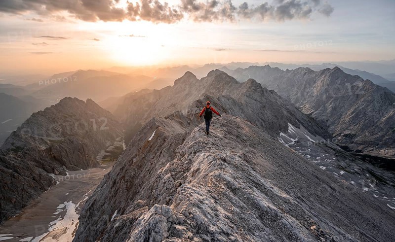 Mountaineer with helmet on a narrow rocky ridge at sunrise, crossing the Jubiläumsgrat, view of Höllental with Höllentalferner and Alpspitze, Wetterstein range, Bavaria, Germany, Europe