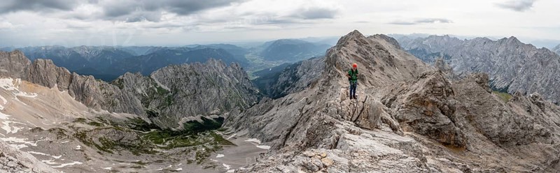 Panorama, mountaineer with helmet on a narrow rocky ridge at sunrise, crossing the Jubiläumsgrat, view of Höllental and Alpspitze, Wetterstein range, Bavaria, Germany, Europe