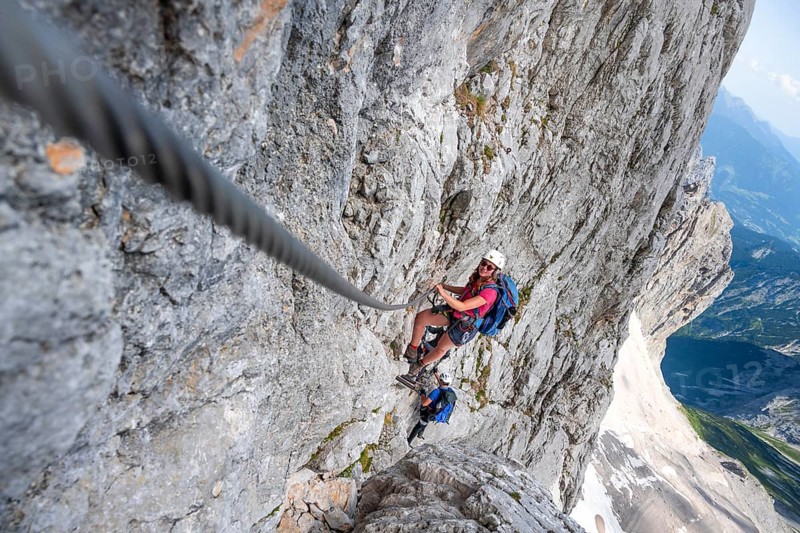 Mountaineer with helmet climbing in a secured via ferrata, Zugspitz via ferrata, ascent to the Zugspitze, view of mountain basin with snowfield of the Höllentalferner and Höllental, Wetterstein range, Wetterstein range, Bavaria, Germany, Europe