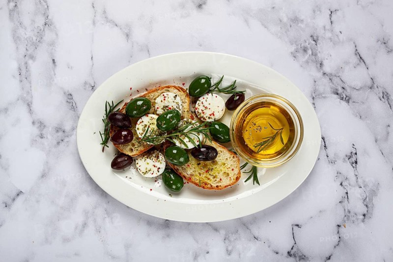 A plate with a snack, ciabatta bread with cheese and olives, olive oil, spices and herbs, top view, no people