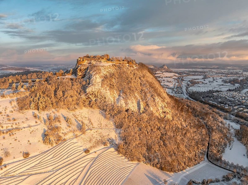 Aerial view of the snow-covered Hegau volcano Hohentwiel with Germany's largest castle ruins on a cold winter morning, at sunrise, in front of it Germany's highest vineyard, the Elisabethenberg at 505 metres above sea level, on the right the town of Singen, on the horizon the neighbouring Hegau volcano Hohenkrähen, district of Constance, Baden-Württemberg, Germany, Europe